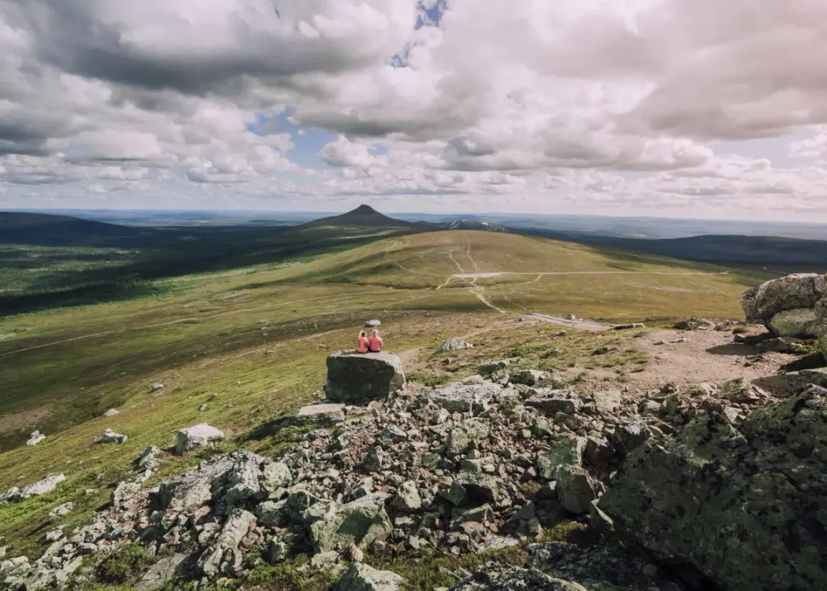 Zwei Wandererinnen genießen die weite Aussicht auf eine Berglandschaft in Schweden. Die Wolkenformationen am Himmel sind dramatisch.