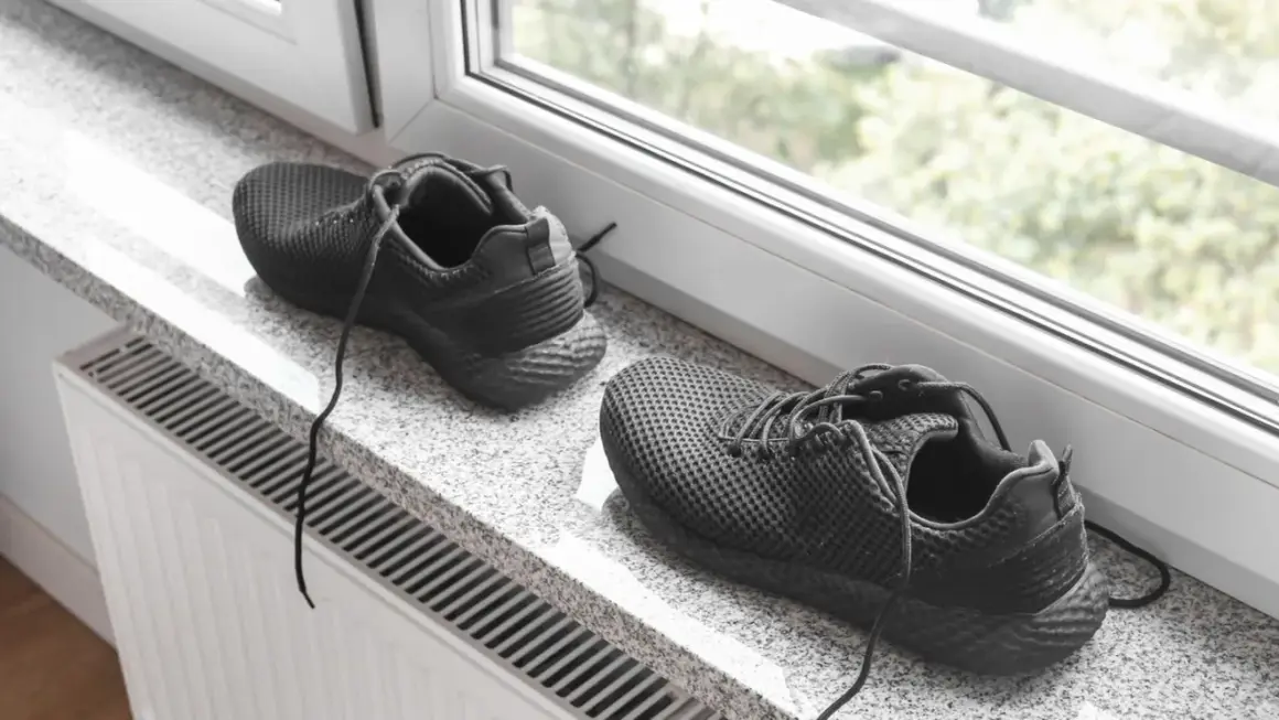 Schwarze Turnschuhe trocknen auf einem Fensterbrett über einer Heizung.