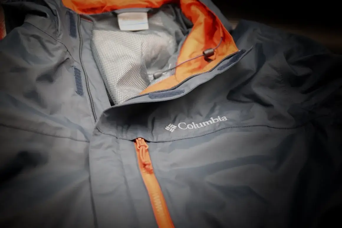 Eine graue Columbia Hardshelljacke mit orangefarbenem Reißverschluss und Kragen. Perfekt für jedes Wetter.