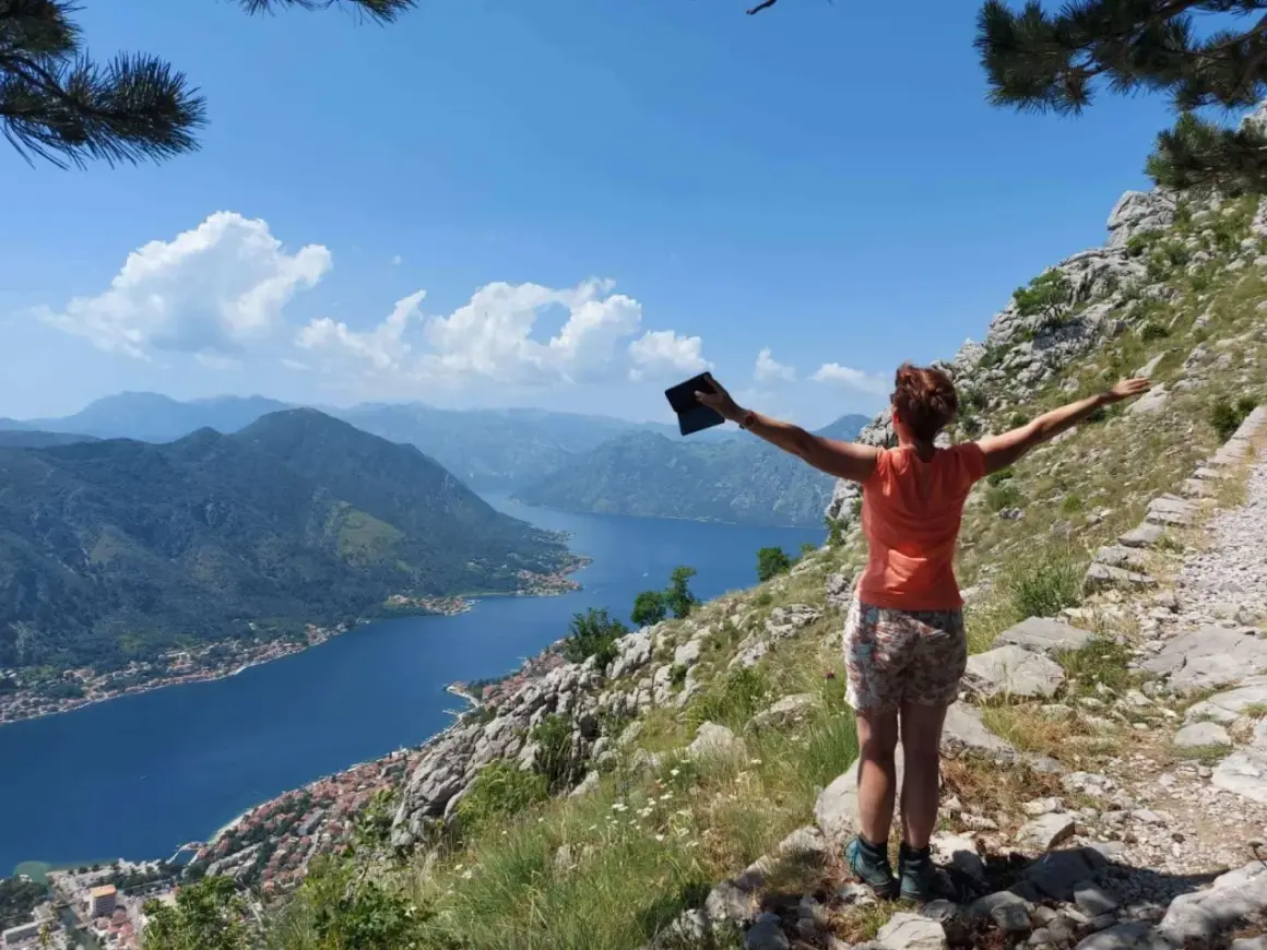 Frau genießt die Aussicht beim **Montenegro wandern**. Der Blick schweift über die Bucht von Kotor, umgeben von Bergen.