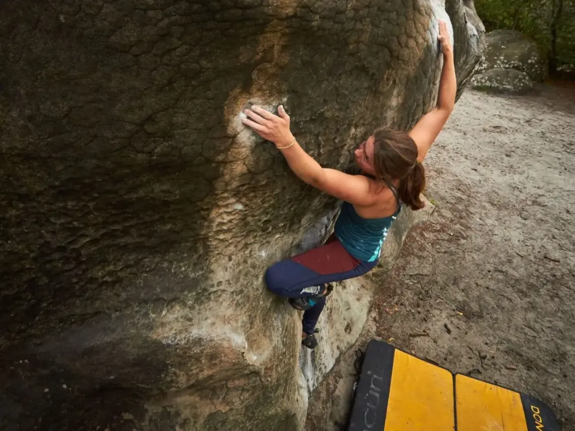Eine Frau klettert an einem Felsen in Fontainebleau. Sie nutzt ihre Kraft und Technik beim Bouldern.