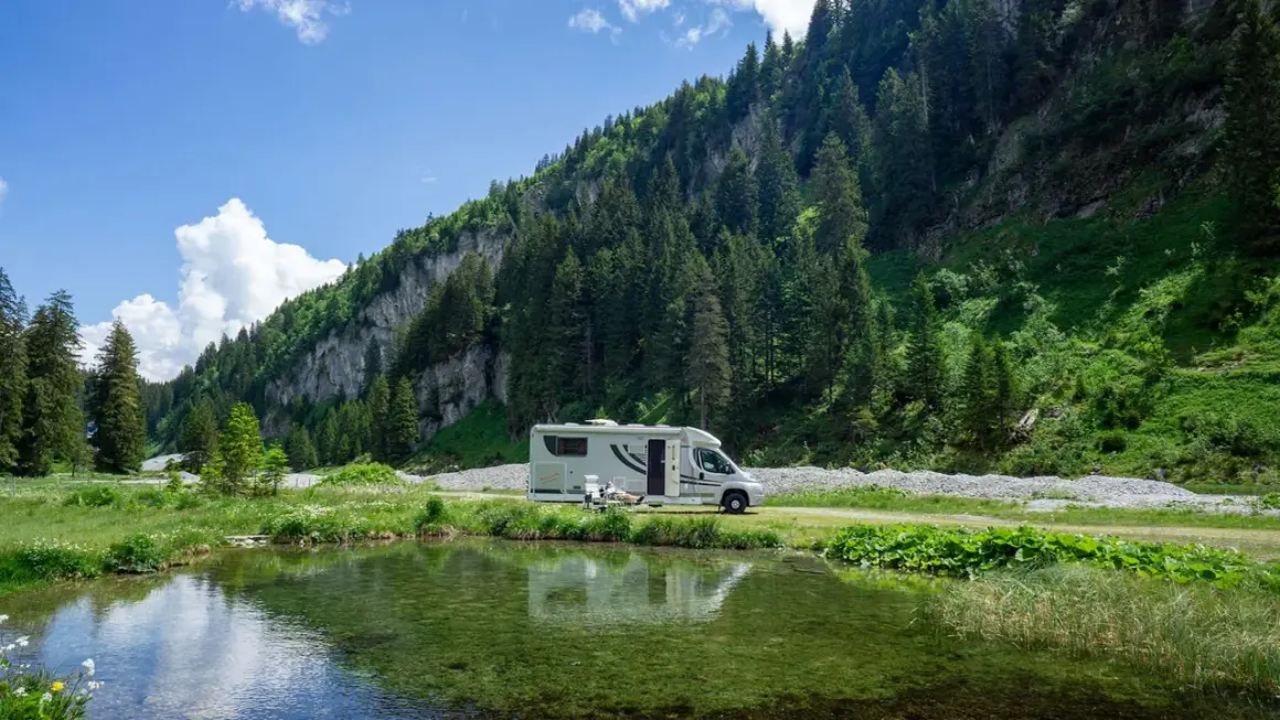 Wohnmobil am Bergsee. Hier darf man in der Schweiz wild campen, umgeben von grünen Hängen und Nadelbäumen.