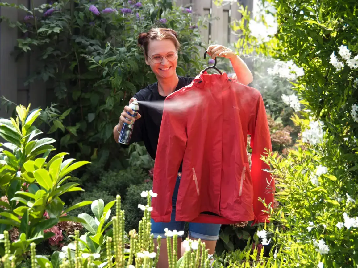 Frau sprüht rote Softshelljacke im Garten ein, um sie zu waschen und zu imprägnieren.