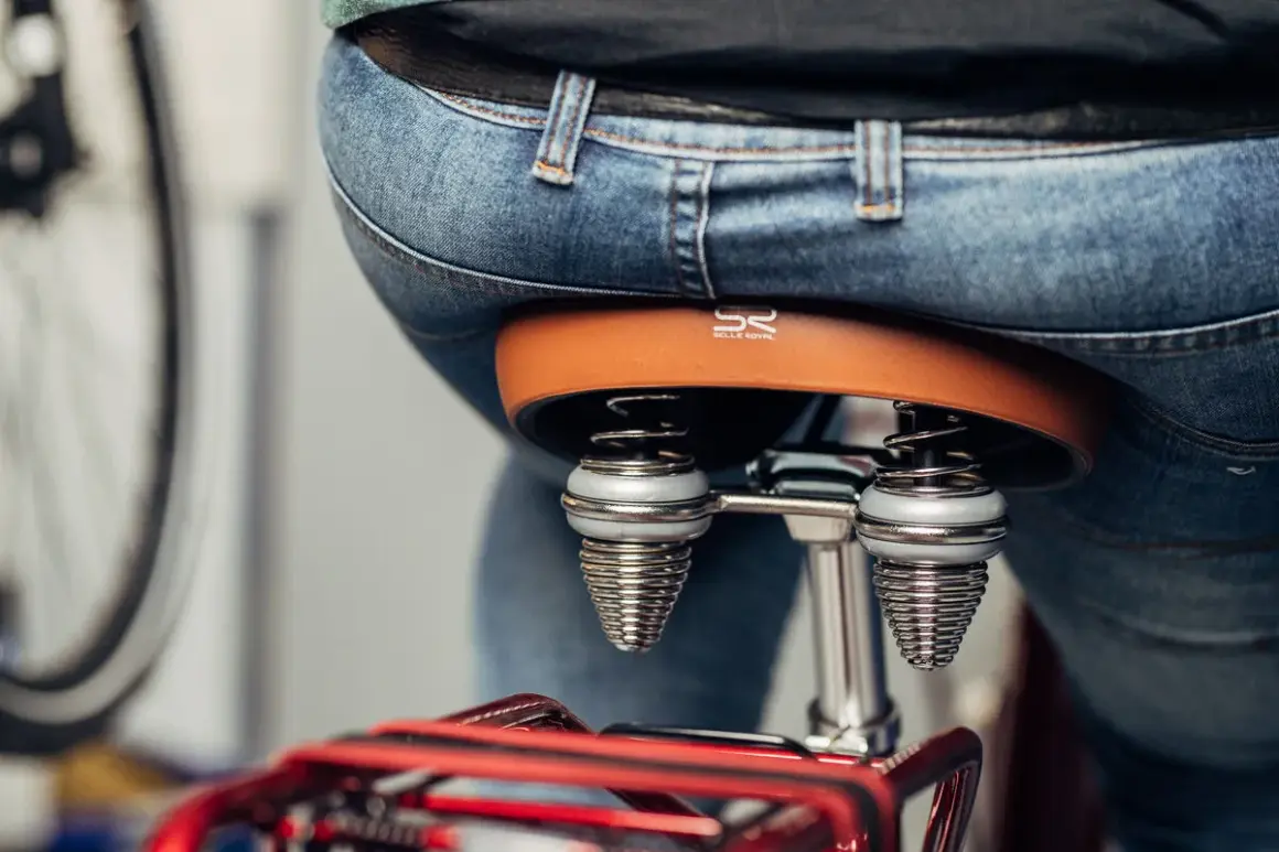 Person sitzt auf einem Fahrradsattel. Der Sattel ist braun und hat Federn. Der Sattel zu breit für Komfort.