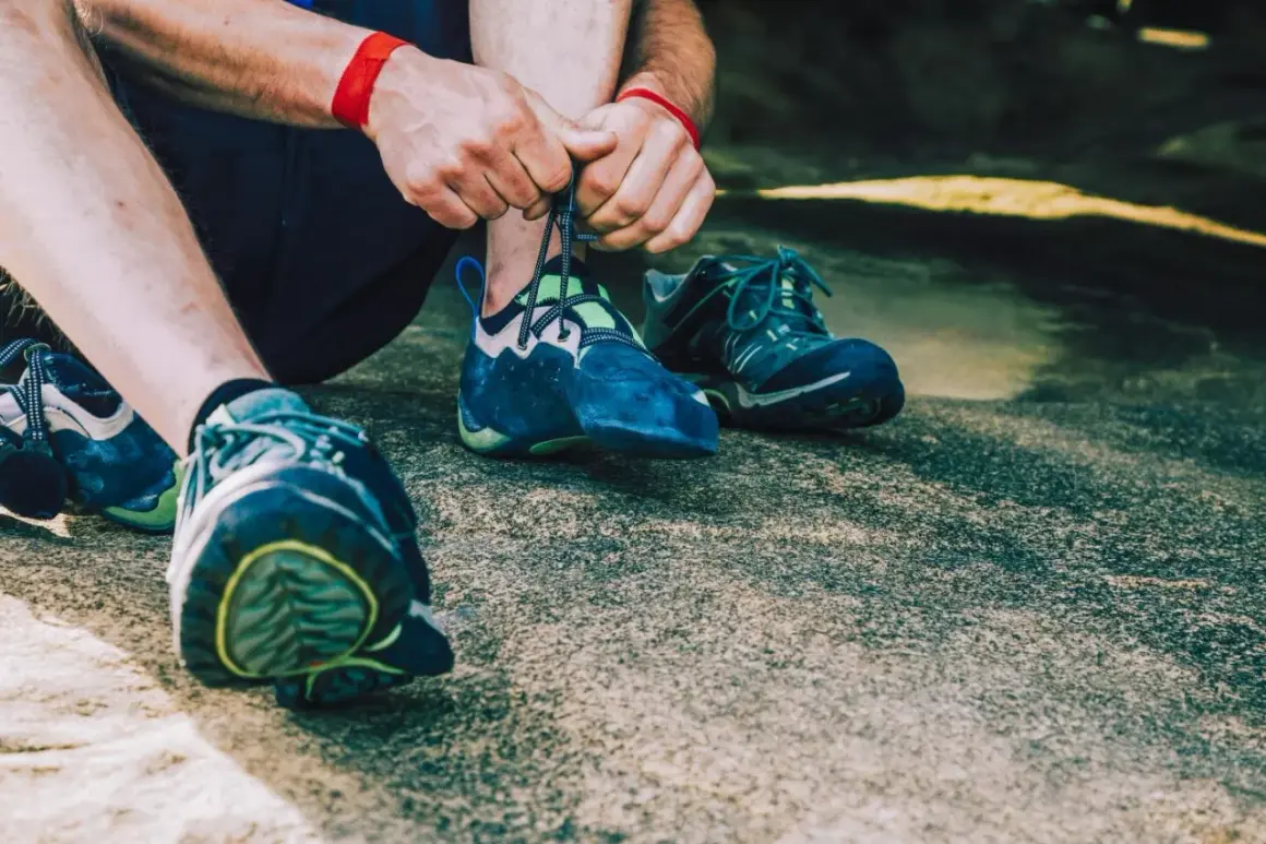 Hände schnüren blaue Kletterschuhe, bereit für den nächsten Aufstieg. Die Füße sind für das Klettern vorbereitet, um die Felsen zu meistern.