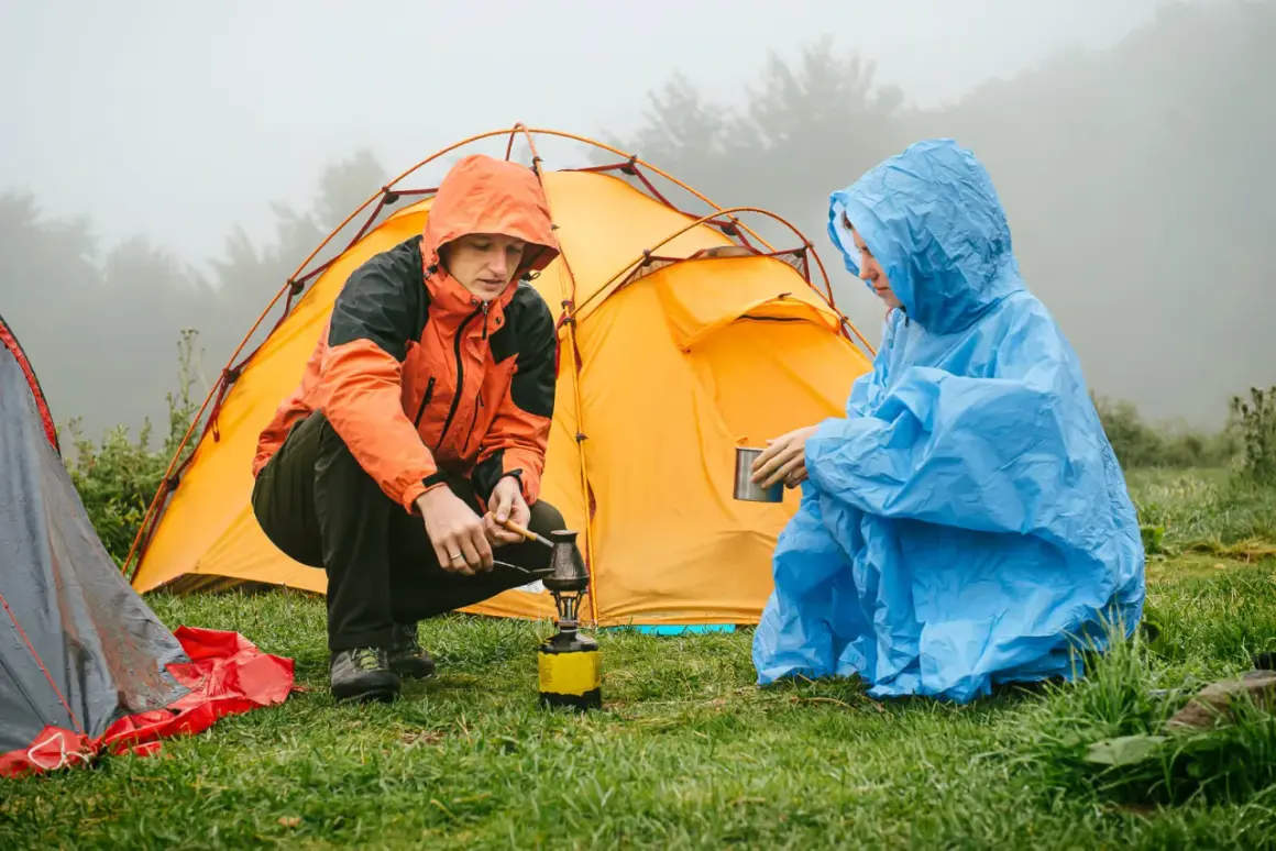 Zwei Camper im Regen bereiten sich eine warme Mahlzeit zu, während das Zelt trocknen muss.