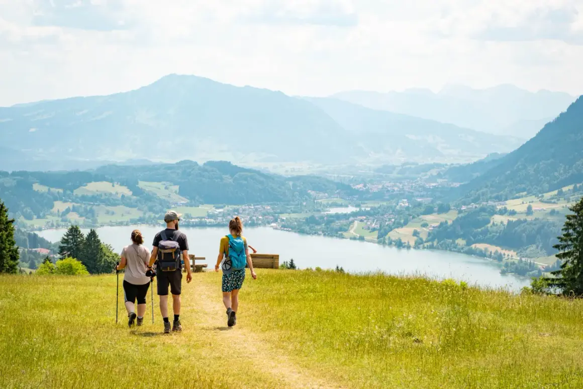 Drei Personen genießen eine leichte Wanderung mit Blick auf einen See und Berge.