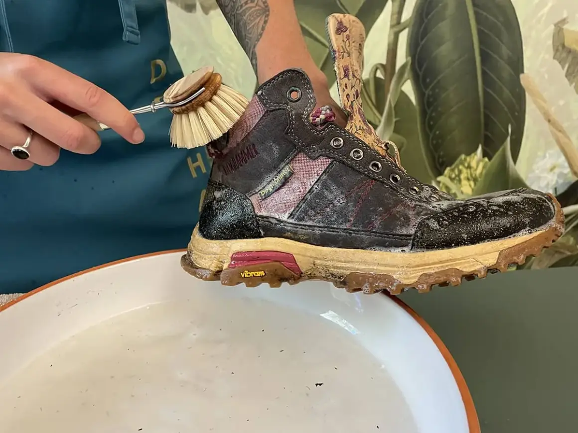 Schmutzige Wanderschuhe reinigen mit einer Bürste und Seifenwasser.