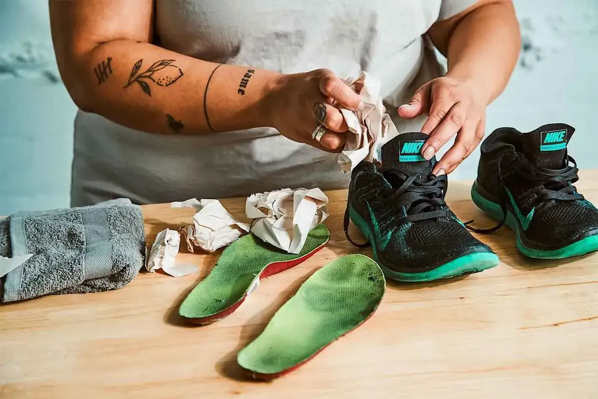 H&auml;nde stopfen Papier in Laufschuhe, um sie zu trocknen. Ein Handtuch und Einlegesohlen liegen daneben.