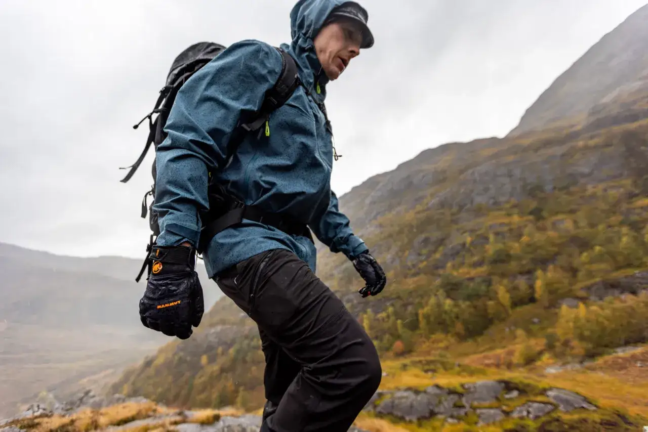 Ein Wanderer in einer blauen Hardshelljacke trotzt dem Regen in den Bergen. Die Jacke schützt ihn vor Nässe und Wind.