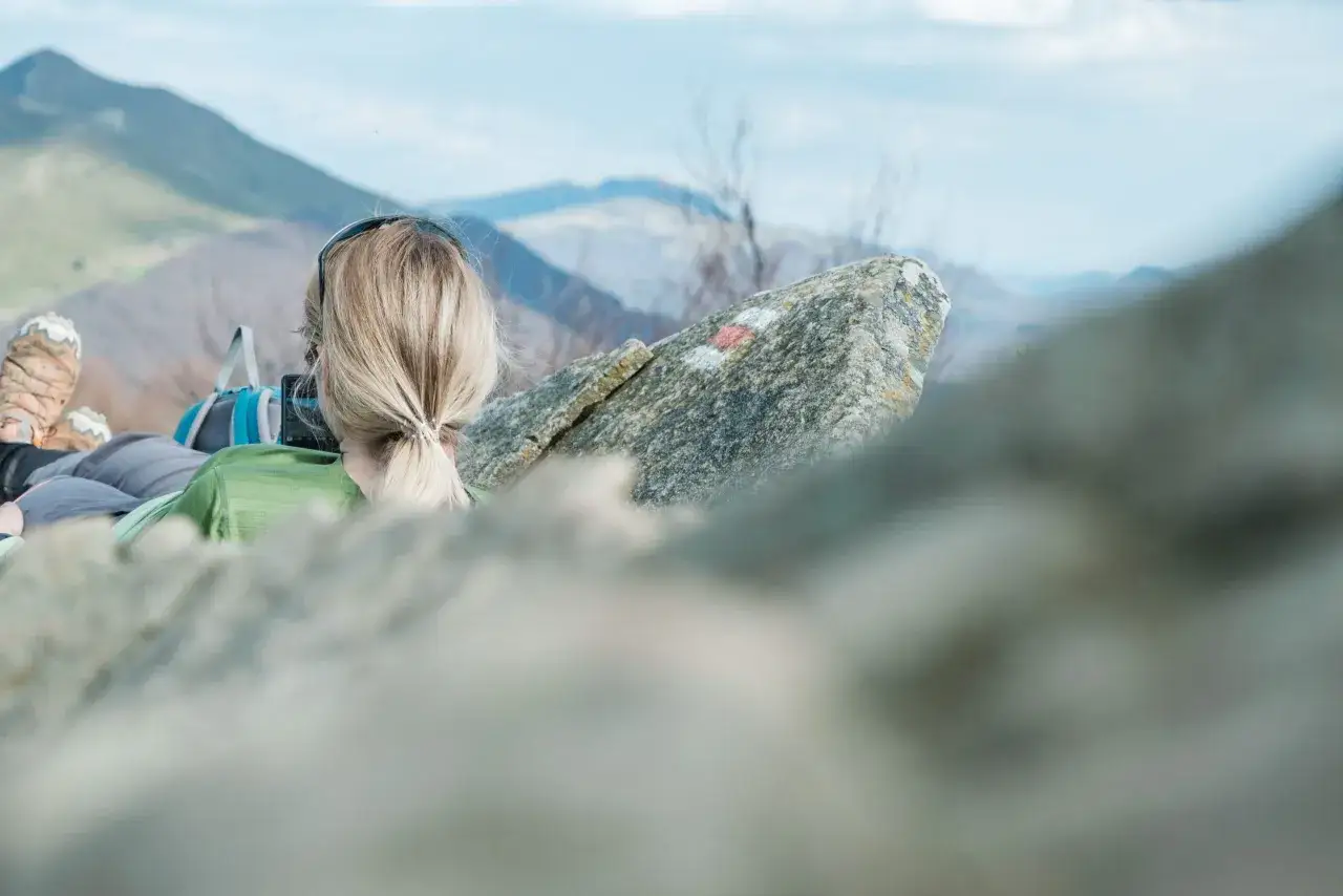 Frau mit blondem Zopf genie&szlig;t die Aussicht beim Wandern in Polen. Bergpanorama und markierter Stein im Vordergrund.