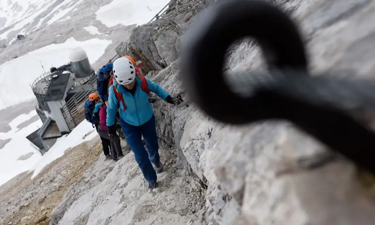 Bergsteiger auf einem felsigen Pfad, die Zugspitze ohne Klettersteig im Blick. Ein Seil sichert den Weg.
