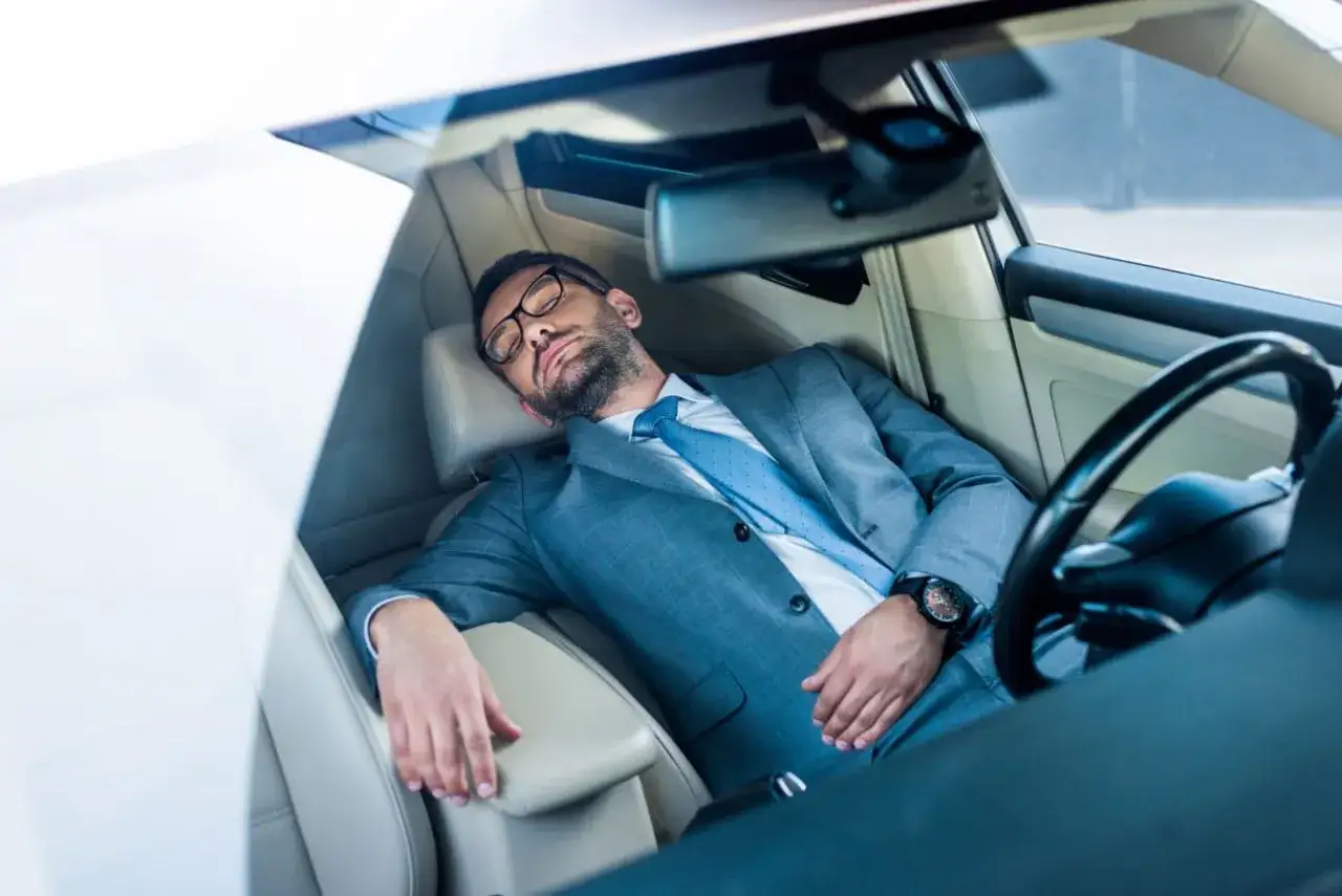 Mann im Anzug schl&auml;ft im Auto. Ob man in Italien im Auto schlafen darf, ist eine andere Frage.