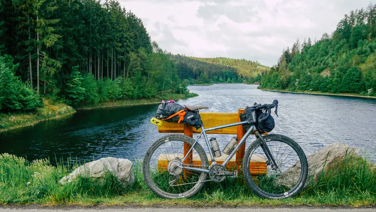Gravelbike mit Gepäcktaschen ruht am Ufer eines Sees, bereit für die nächste Bikepacking tour durch den grünen Wald.