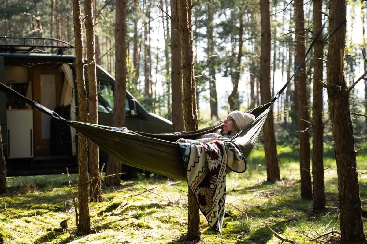 Frau entspannt in Hängematte im Wald, neben einem Campervan. Hier ist ein Beispiel, wo ist wildcampen erlaubt.