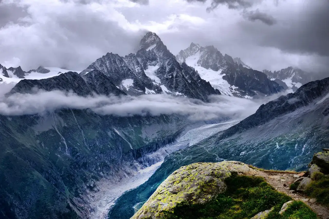 Dramatische Berglandschaft mit Gletscher und Wolken. Ein Pfad schlängelt sich durch die Szenerie, ideal für weitwanderwege europa.