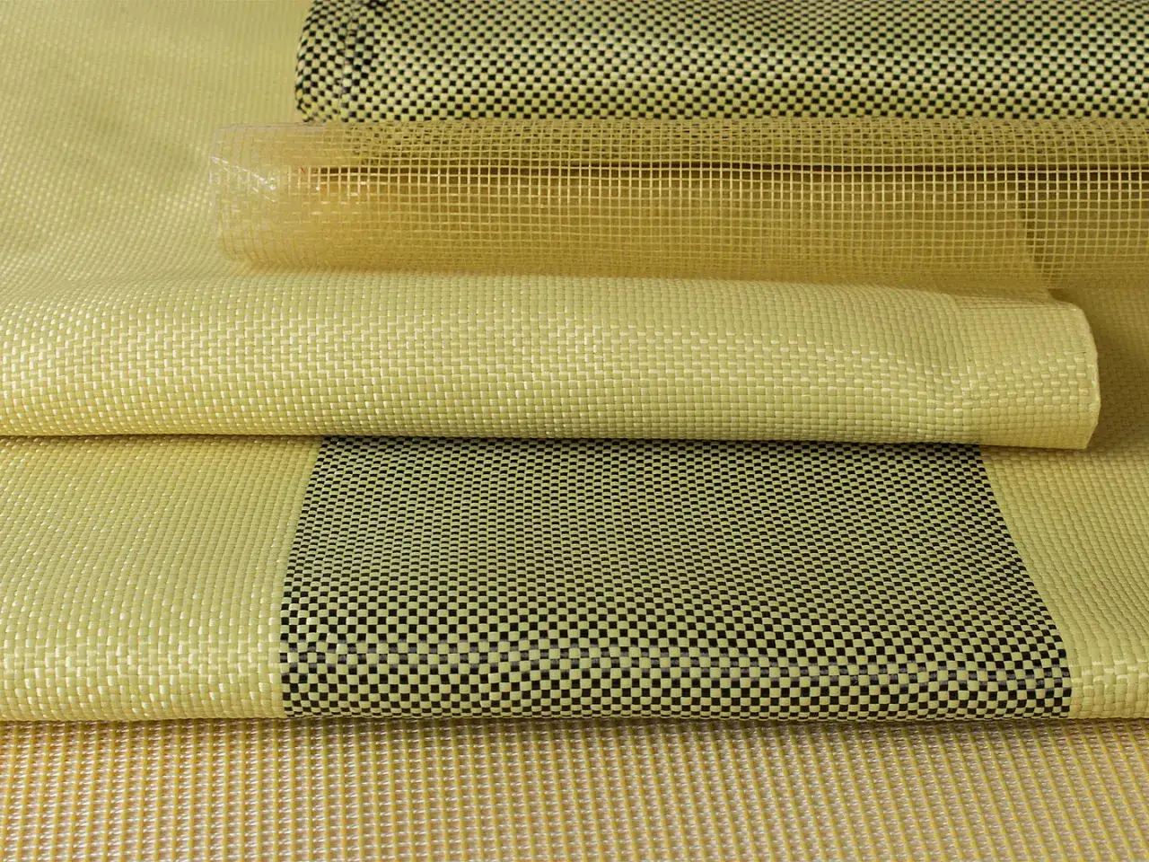 Stapel von gelbem Gewebe, darunter ein aufgerolltes Stück mit kariertem Muster. Dies ist ein Beispiel für die Stärke von Aramid.