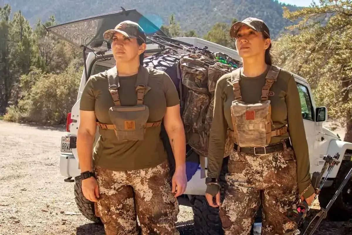Zwei J&auml;gerinnen in Tarnkleidung stehen vor einem Jeep. Ihre Kleidung, die auch Baumwolle enth&auml;lt, ist atmungsaktiv und ideal f&uuml;r die Jagd.