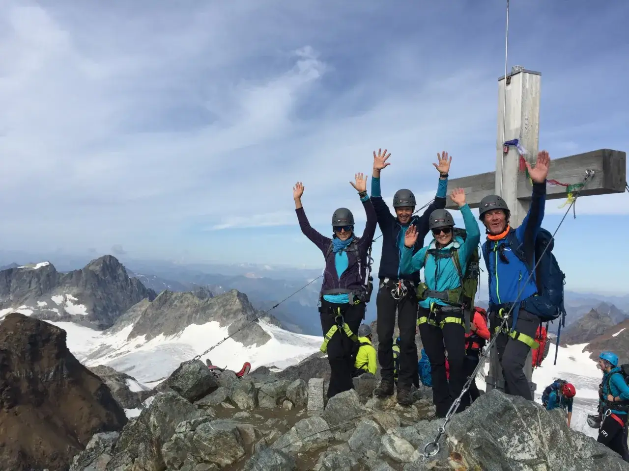 Vier gl&uuml;ckliche Bergsteiger feiern den Gipfelsieg am Piz Buin, umgeben von alpiner Weite.