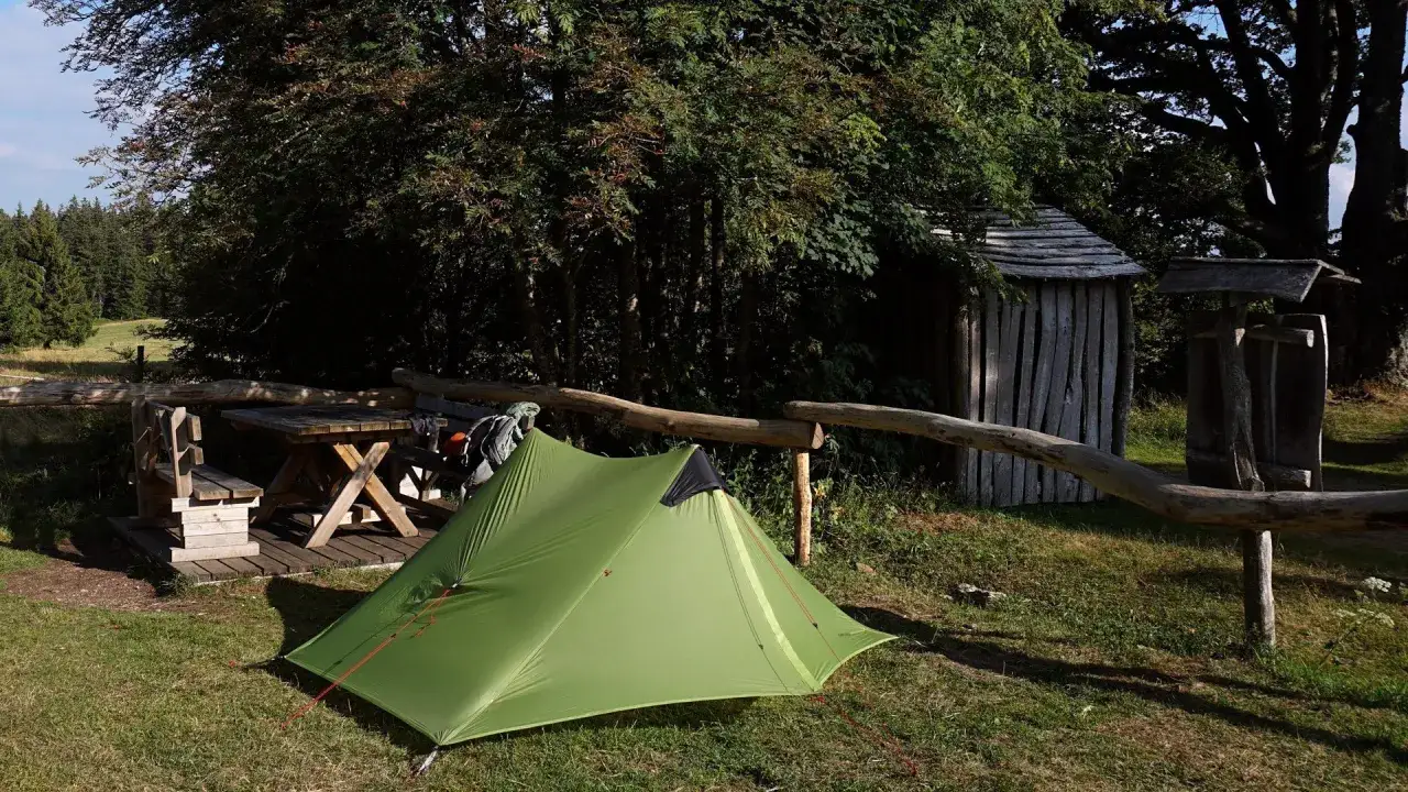Grünes Zelt und Holzbank mit Tisch laden zum Biwak ein. Die Bedeutung von Biwak: Natur genießen, abschalten.