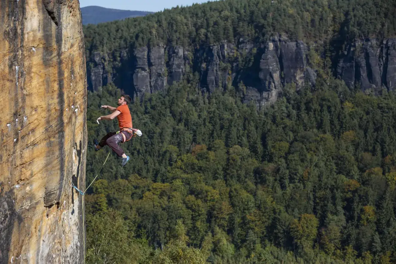 Ein Mann klettert an einer Felswand in Tschechien. Im Hintergrund erstreckt sich ein dichter, gr&uuml;ner Wald.