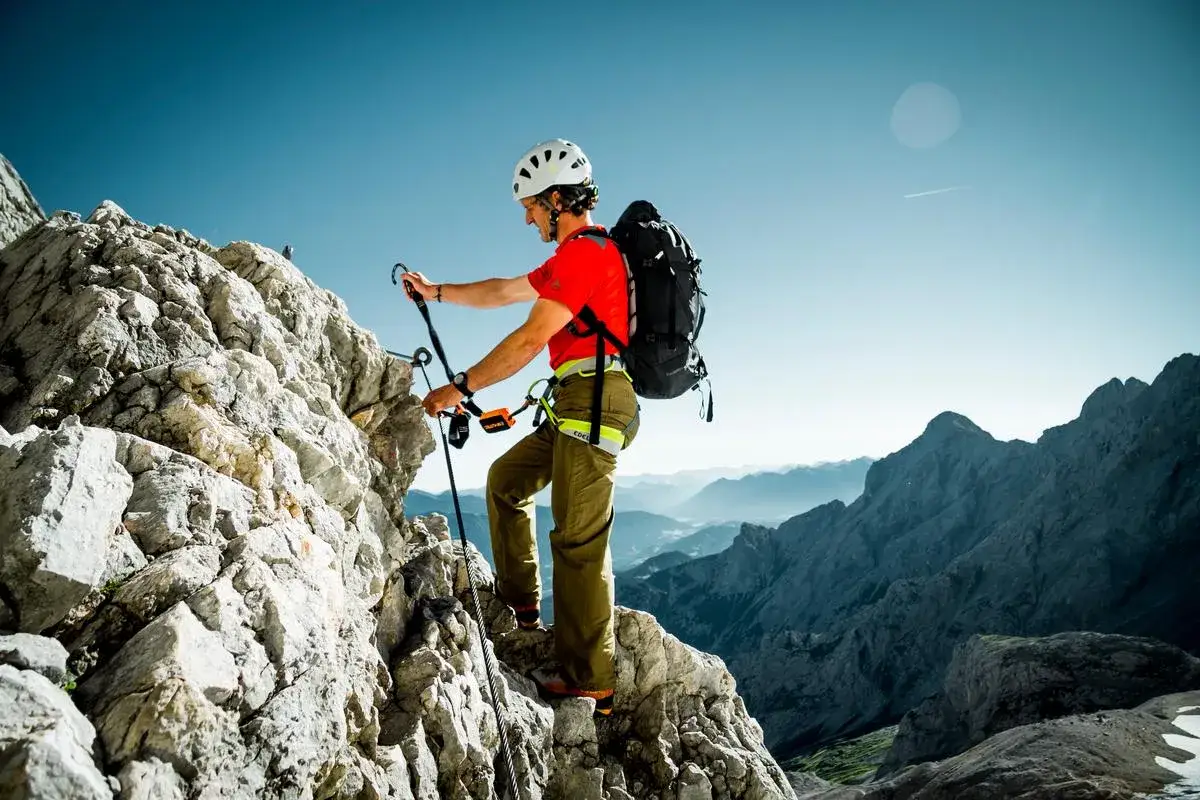 Mann klettert gesichert über Felsen. Seine Packliste für den Klettersteig ist komplett: Helm, Gurt, Seil und Rucksack.