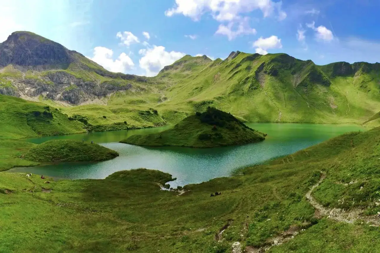 Gr&uuml;ne H&uuml;gel umgeben einen t&uuml;rkisfarbenen See. Eine kleine Insel ragt aus dem Wasser. Perfekt f&uuml;r eine Schrecksee Wanderung.