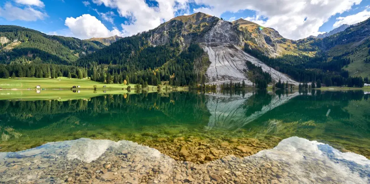 Spiegelglatter See im Tannheimer Tal, umgeben von gr&uuml;nen H&auml;ngen und bewaldeten Bergen. Ein versteckter Ort, der zu den sch&ouml;nsten Tannheimer Tal Geheimtipps z&auml;hlt.