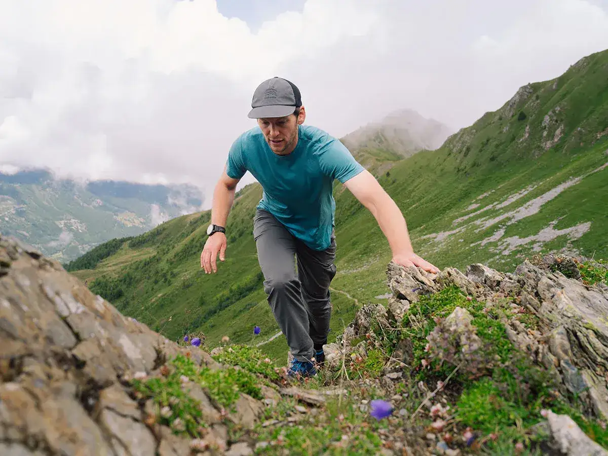 Mann klettert bergauf, genie&szlig;t die Aussicht. Sein Shirt aus Merinowolle bietet Komfort und Atmungsaktivit&auml;t &ndash; ein klarer Vorteil f&uuml;r jede Tour.