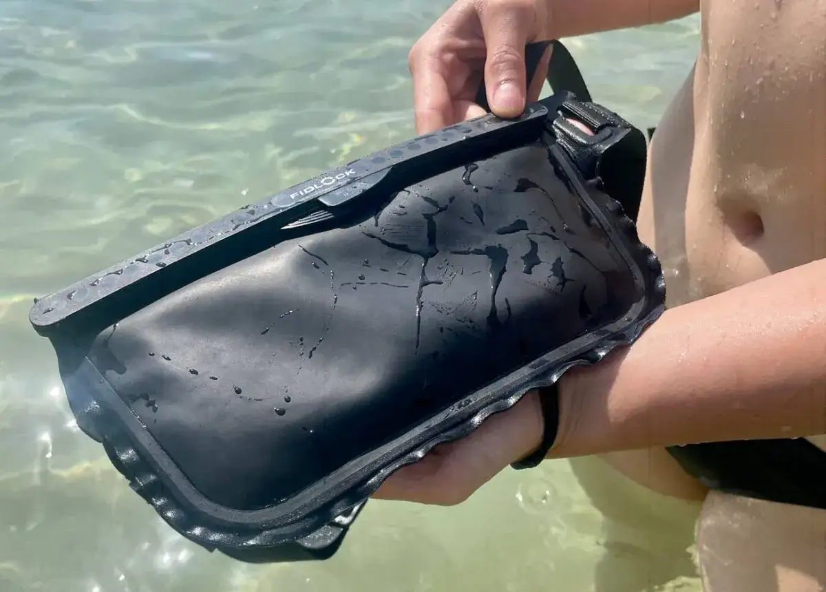 Schwarze Tasche mit Fidlock-Verschluss im Wasser. Perfekt für den Strand, um den Unterschied zwischen wasserdicht und wasserfest zu demonstrieren.