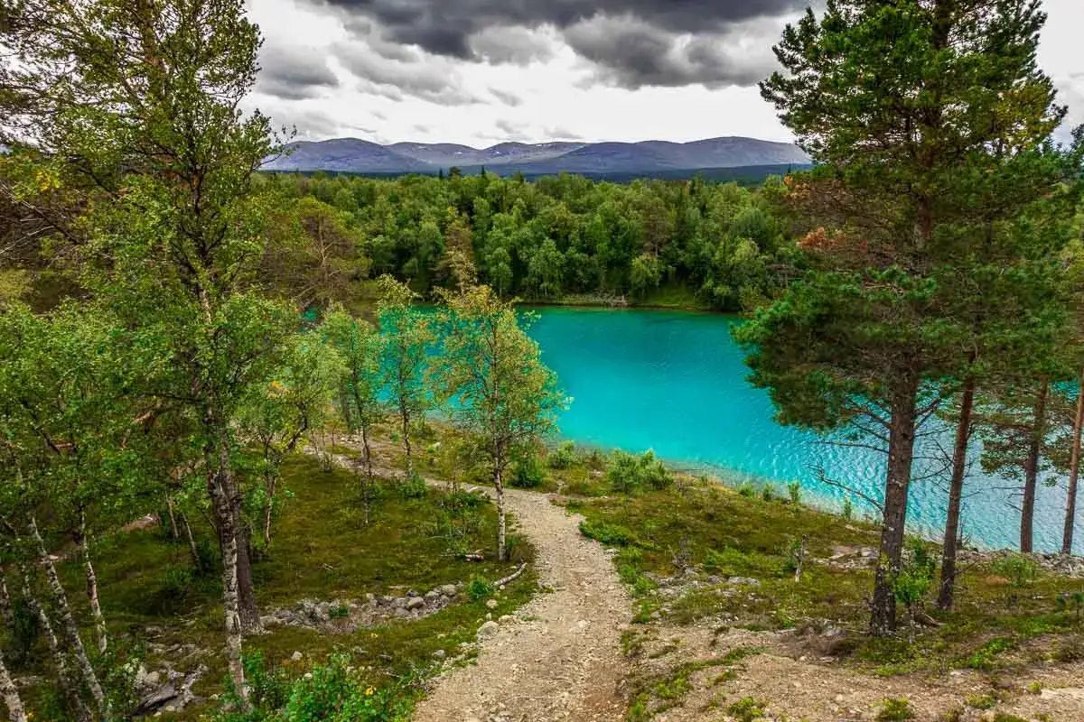 Ein Pfad führt zu einem türkisfarbenen See, umgeben von grünen Wäldern und Bergen. Perfekt für fernwanderwege schweden.