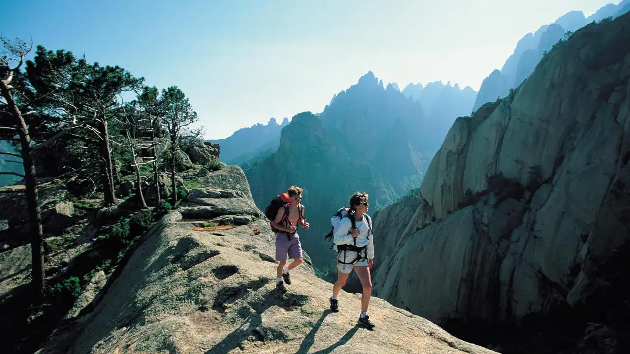 Zwei Wanderer auf einem felsigen korsika wanderweg mit dramatischen Bergformationen im Hintergrund.