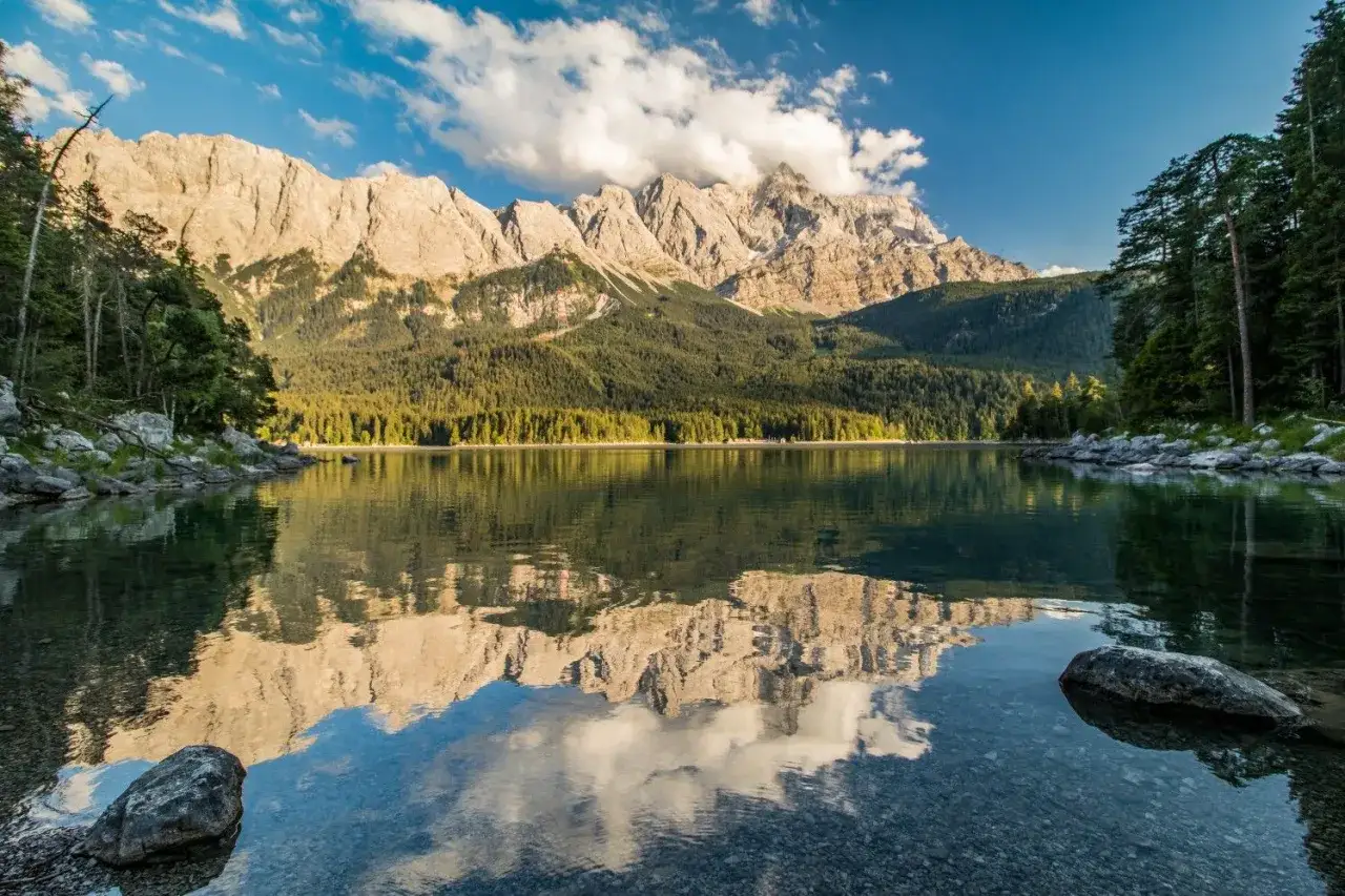 Spiegelglatter Eibsee mit Bergpanorama und Wald. Der Eibsee Rundweg bietet diese Aussicht.