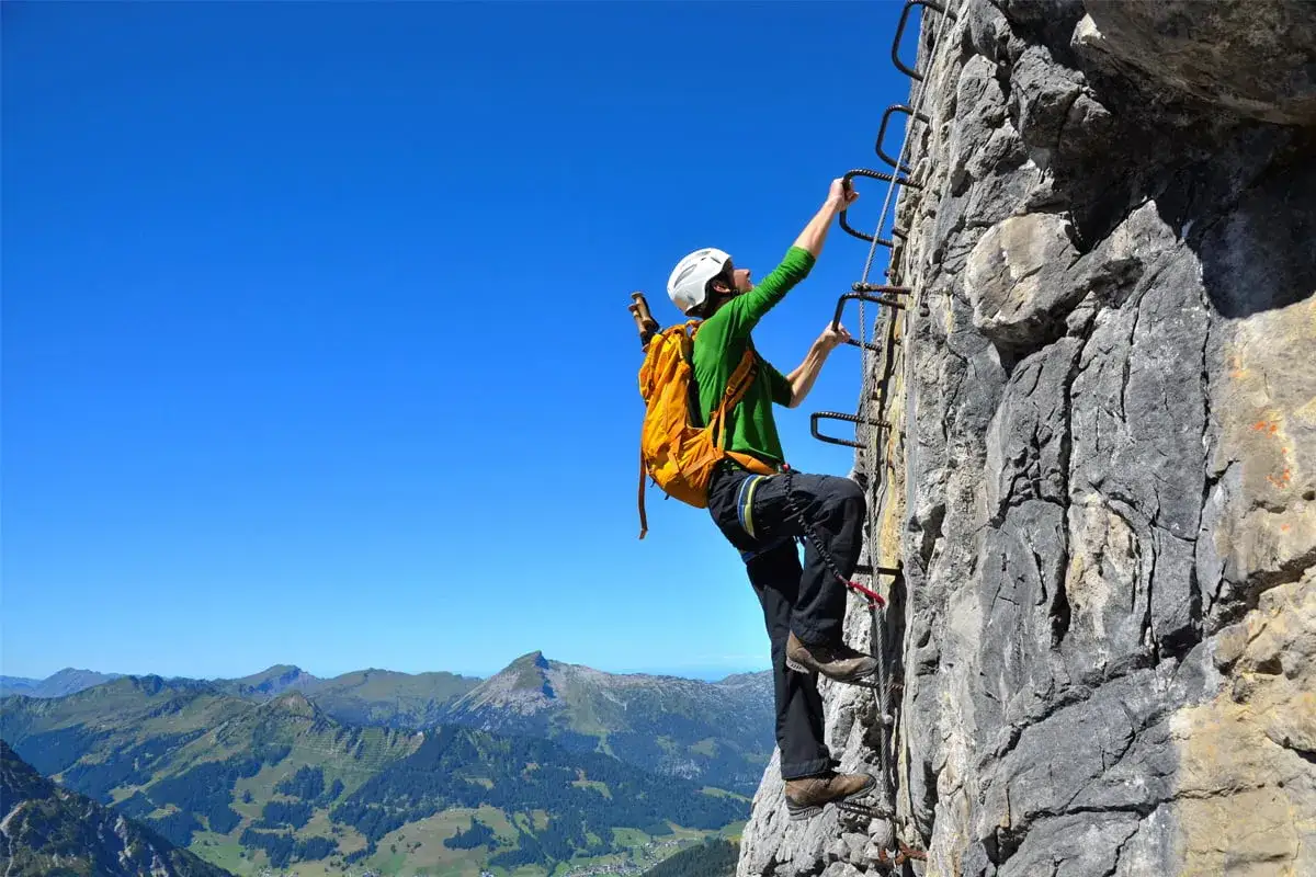 Bergsteiger erklimmt den Mindelheimer Klettersteig, gesichert an einem Stahlseil, mit Alpenpanorama im Hintergrund.
