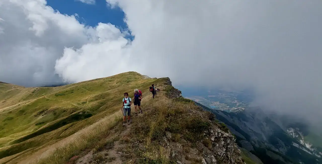 Wanderer auf einem schmalen, hohen Gratpfad, der sich durch gr&uuml;ne H&uuml;gel schl&auml;ngelt, mit Wolken, die die Aussicht auf das Tal verdecken.