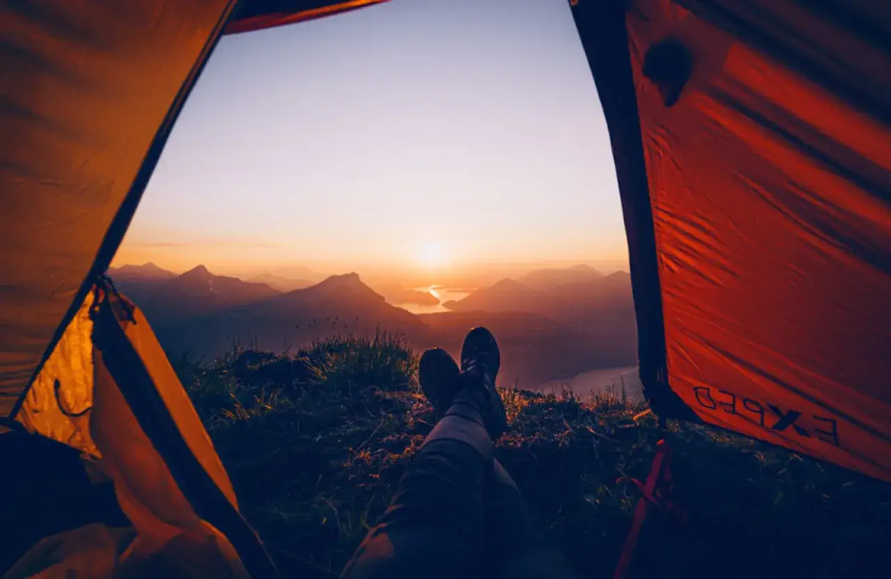 Blick aus dem Zelt auf einen Sonnenuntergang über Bergen und See. Hier darf man in der Schweiz wild campen und die Natur genießen.