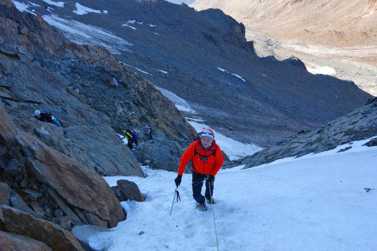 Bergsteiger in orangefarbener Jacke kämpft sich auf Schnee und Eis den Hang hinauf. Die Wildspitze Besteigung ist eine Herausforderung.