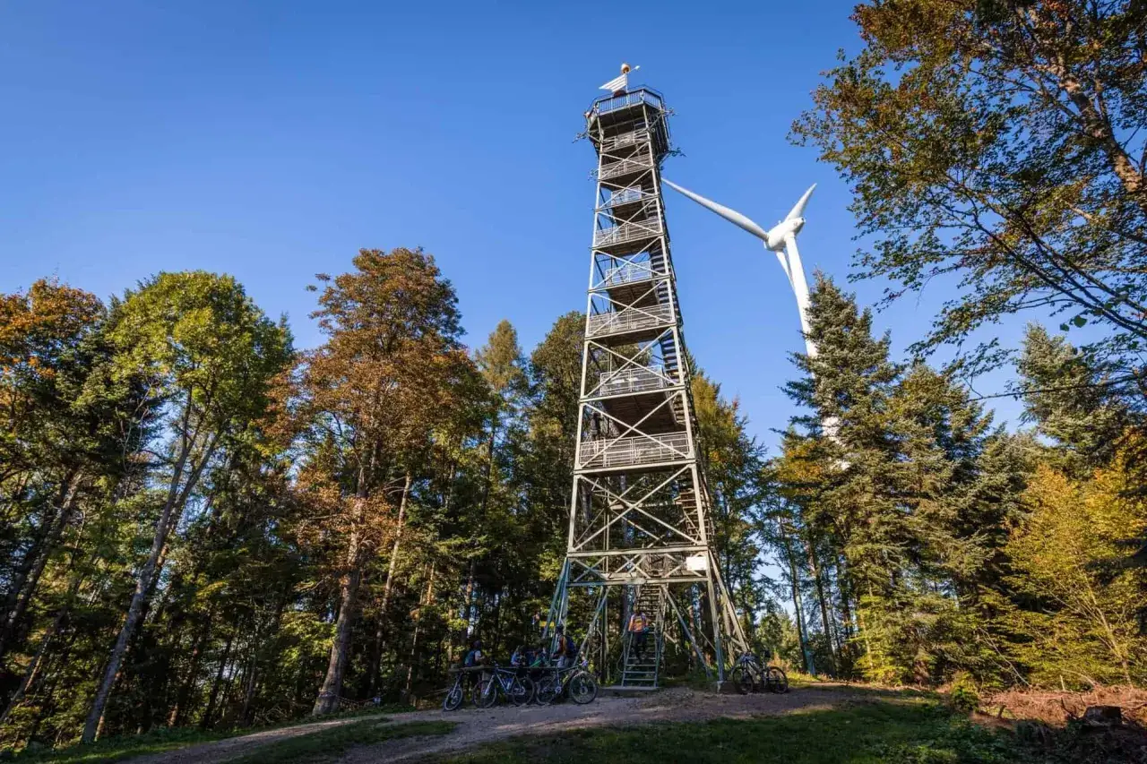 Aussichtsturm am Rosskopf Freiburg mit Windrad im Hintergrund. Radfahrer warten auf den Aufstieg.