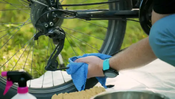 Mann reinigt die Fahrradkette mit einem blauen Tuch. So wird das Fahrradfahren wieder leichtgängig.