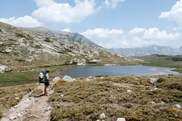 Wanderer auf dem GR20, Korsika, auf dem Weg zu einer Hütte. Bergsee und felsige Landschaft.