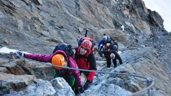 Bergsteiger seilen sich auf dem Weg zur Wildspitze ab. Ein Mann im roten Anzug lächelt in die Kamera.