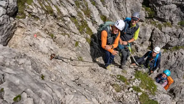 Vier Wanderer genießen den **Mindelheimer Klettersteig**. Ein Stahlseil sichert den Weg über felsiges Gelände.
