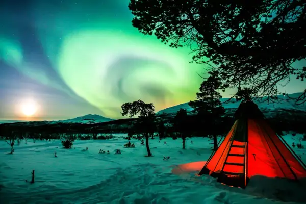 Ein leuchtend rotes Zelt steht im Schnee unter dem Nordlicht. Perfektes **Wildcampen Skandinavien** Erlebnis.