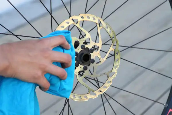 Hand reinigt goldene Fahrrad-Scheibenbremse mit blauem Tuch. Perfekt für den Wechsel der Scheibenbremse am Fahrrad.