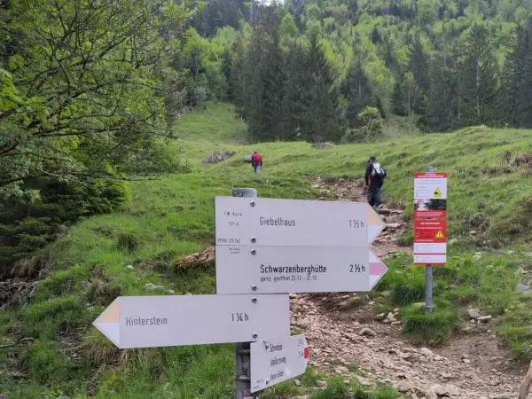 Wegweiser für eine Schrecksee Wanderung: Giebelhaus, Schwarzenberghütte und Hinterstein sind Ziele. Wanderer steigen bergauf.
