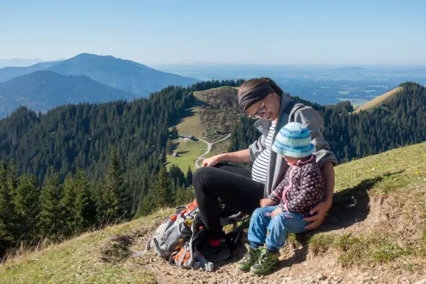 Schwangerschaft und Wandern: Eine Frau mit Babybauch und Kind genießen die Aussicht auf Berge und Wälder.