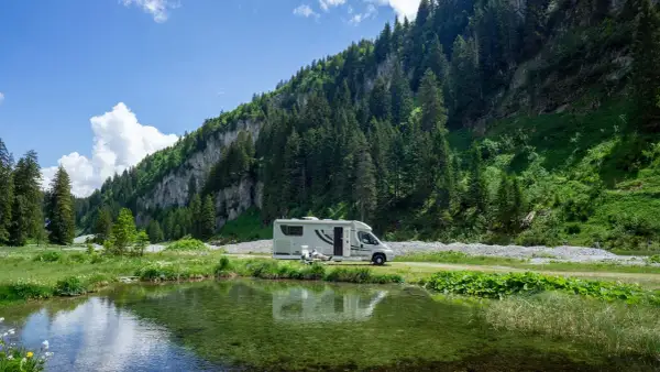 Wohnmobil am Bergsee. Hier darf man in der Schweiz wild campen, umgeben von grünen Hängen und Nadelbäumen.