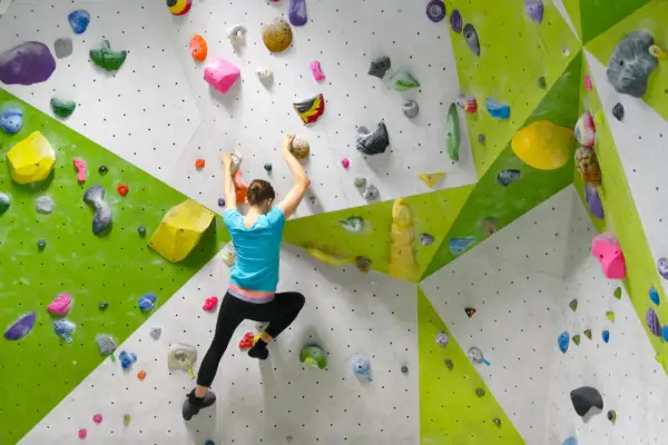 Eine Frau klettert an einer bunten Boulderwand. Sie greift nach Griffen, um sich hochzuziehen. Das ist, was ist bouldern: Klettern ohne Seil in Absprunghöhe.