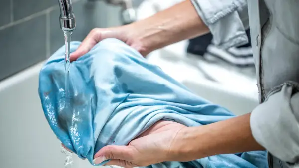 Hände spülen Matsch aus Kleidung unter fließendem Wasser.