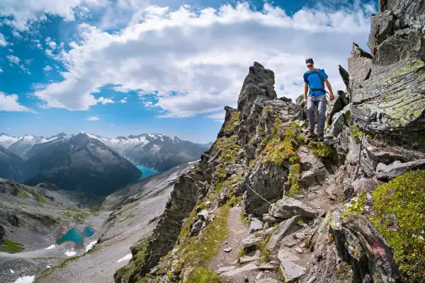 Wanderer auf einem steinigen Pfad der Peter Habeler Runde mit Blick auf türkisfarbene Bergseen und schneebedeckte Gipfel.